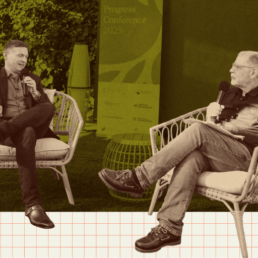 Two men sit on outdoor chairs holding microphones, engaged in conversation at an event. A conference sign is visible in the background.